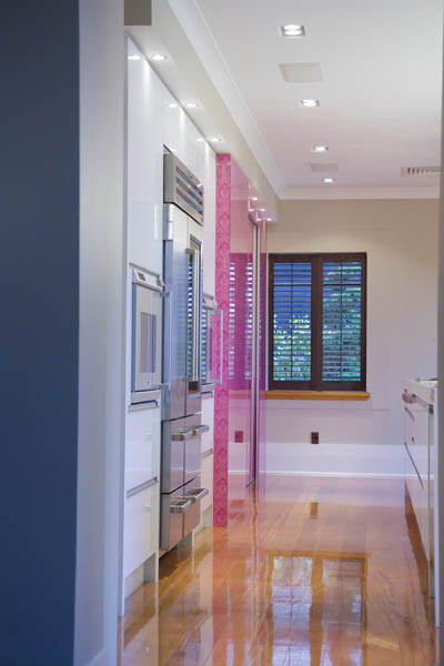 Idée de décoration pour une grande cuisine parallèle minimaliste avec un placard à porte plane, un plan de travail en quartz modifié, une crédence rose, une crédence en feuille de verre, un électroménager en acier inoxydable, parquet clair et îlot.