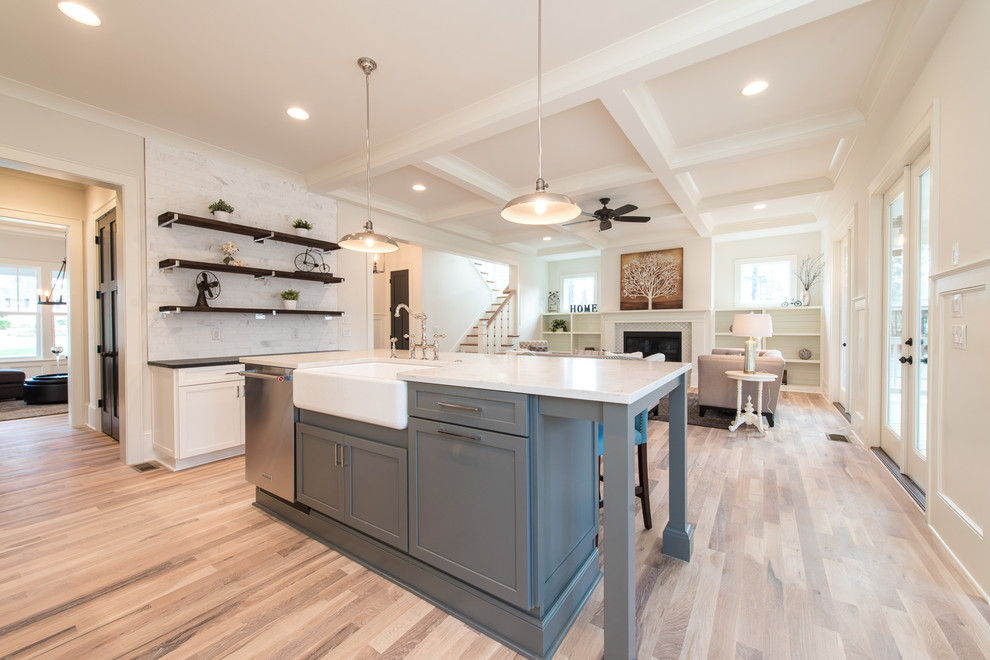 Design ideas for a large traditional l-shaped open plan kitchen in Charlotte with a belfast sink, engineered stone countertops, white splashback, stainless steel appliances, light hardwood flooring, an island and beige floors.