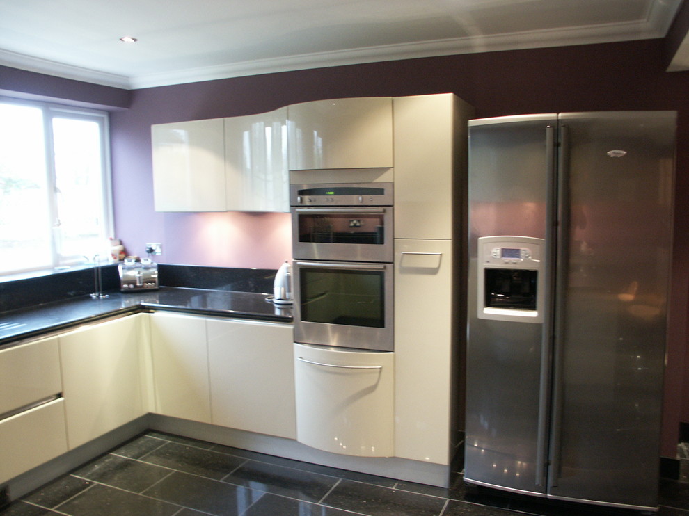 Photo of a medium sized contemporary u-shaped kitchen/diner in Berkshire with an integrated sink, flat-panel cabinets, white cabinets, granite worktops, stainless steel appliances, porcelain flooring and a breakfast bar.