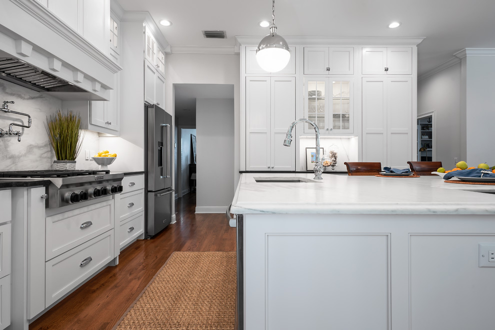 Inspiration for a medium sized classic u-shaped enclosed kitchen in Tampa with a submerged sink, recessed-panel cabinets, white cabinets, marble worktops, white splashback, marble splashback, stainless steel appliances, dark hardwood flooring, an island, brown floors and white worktops.