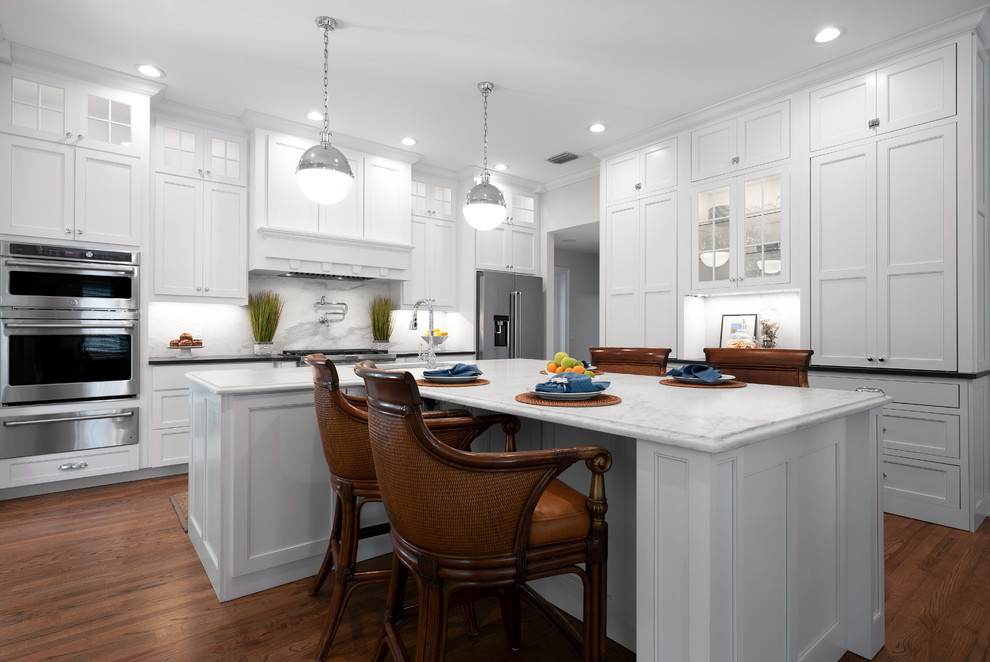 Mid-sized elegant u-shaped dark wood floor and brown floor enclosed kitchen photo in Tampa with an undermount sink, recessed-panel cabinets, white cabinets, marble countertops, white backsplash, marble backsplash, stainless steel appliances, an island and white countertops