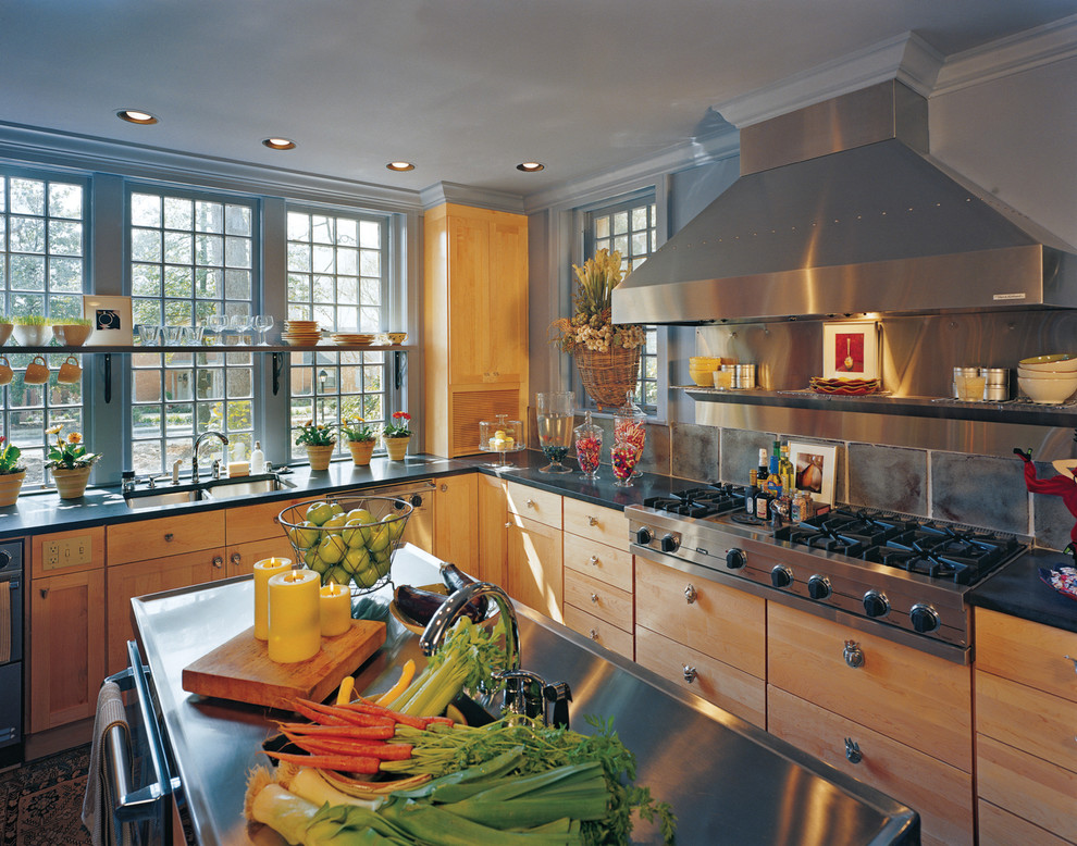 Klassisk inredning av ett kök, med en dubbel diskho, skåp i ljust trä, grått stänkskydd, rostfria vitvaror och en köksö