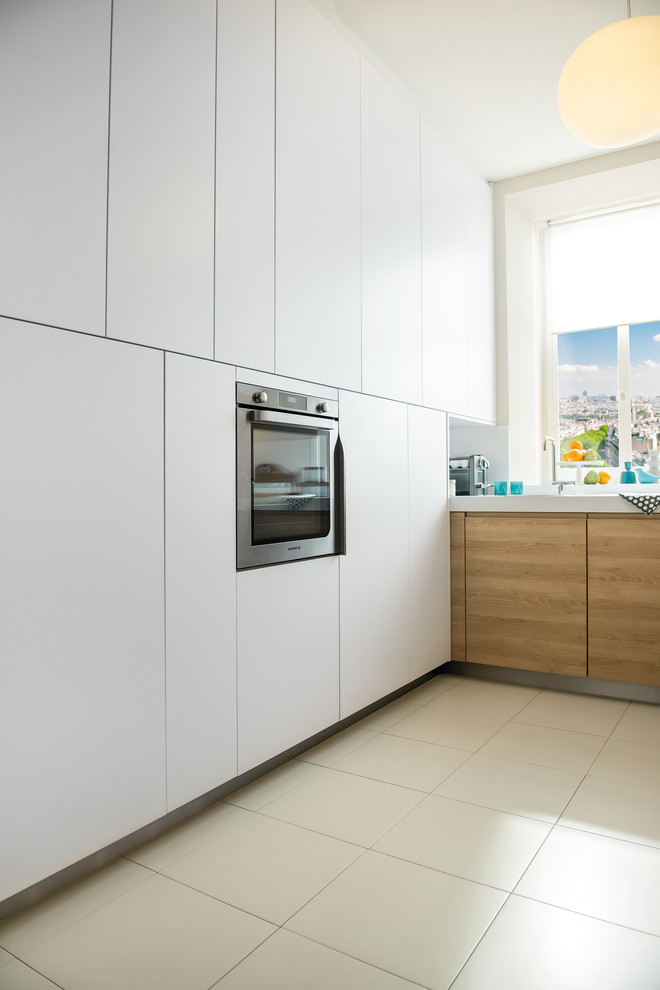 This is an example of a small contemporary l-shaped kitchen in London with a single-bowl sink, white splashback, glass sheet splashback, stainless steel appliances, ceramic flooring and light wood cabinets.