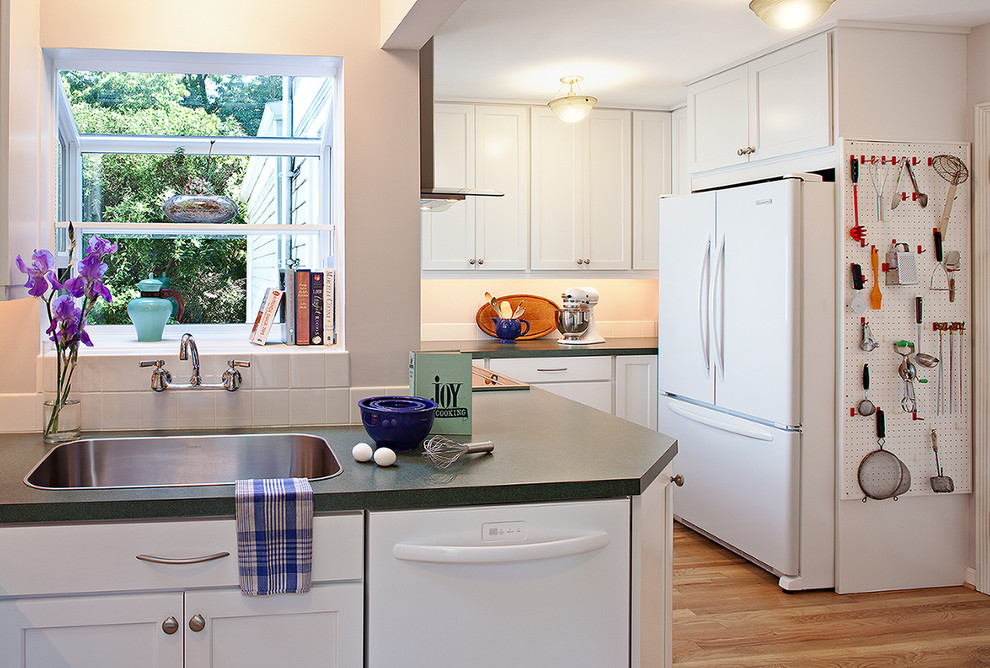 Moderne Küche mit weißen Elektrogeräten, Einbauwaschbecken, weißen Schränken und hellem Holzboden in Seattle
