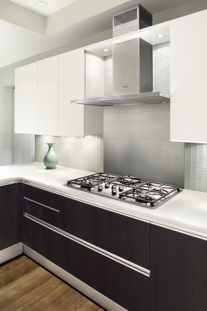 На фото: кухня в стиле модернизм с плоскими фасадами, белым фартуком, фартуком из стеклянной плитки и черно-белыми фасадами с