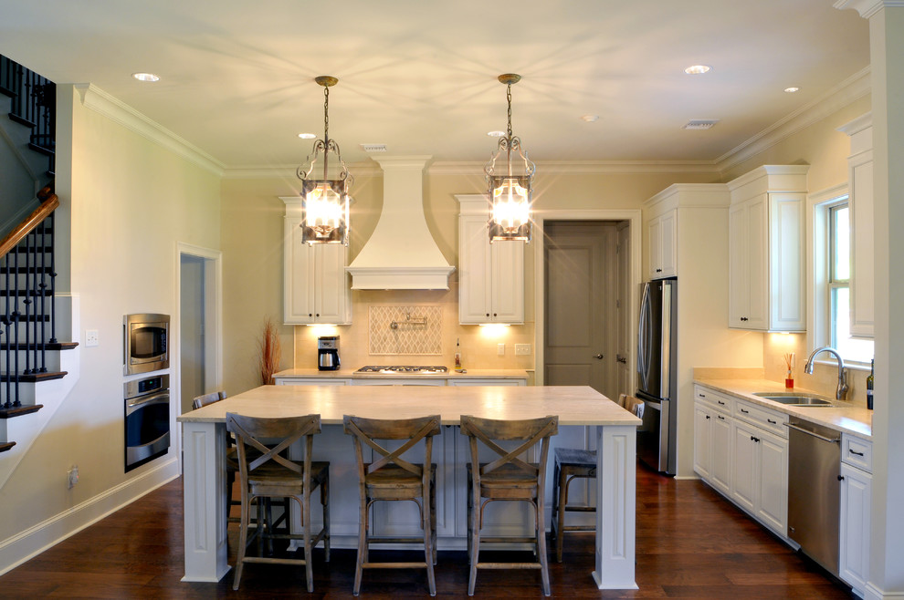Inspiration for a mid-sized timeless l-shaped medium tone wood floor eat-in kitchen remodel in New Orleans with an undermount sink, raised-panel cabinets, white cabinets, limestone countertops, beige backsplash, stone tile backsplash, stainless steel appliances and an island