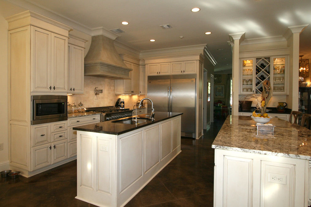 Klassisk inredning av ett mellanstort kök, med en undermonterad diskho, luckor med upphöjd panel, beige skåp, granitbänkskiva, beige stänkskydd, stänkskydd i stenkakel, rostfria vitvaror, betonggolv och en köksö