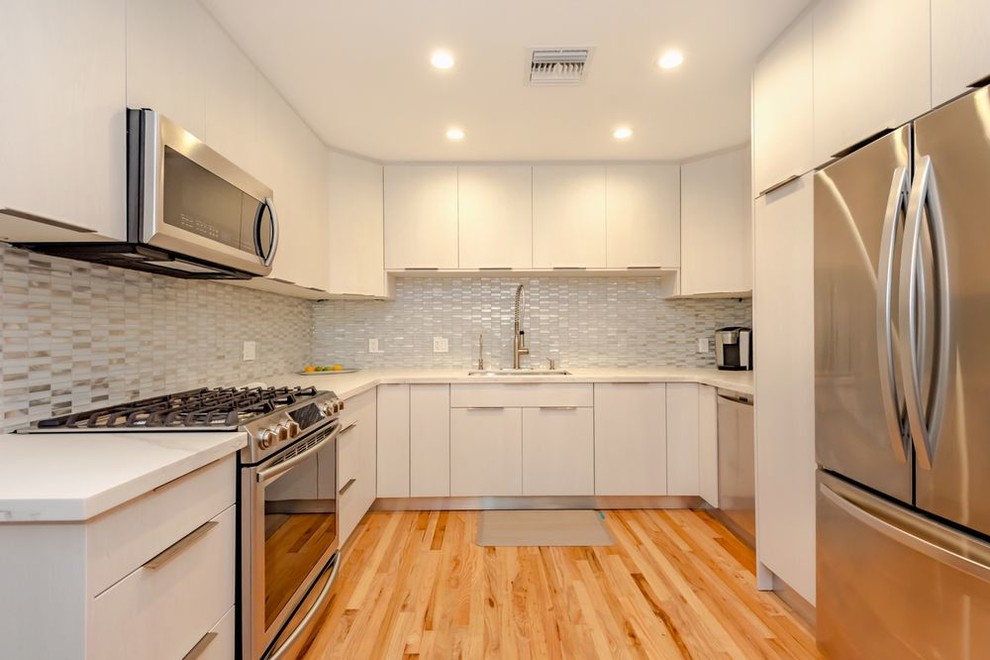 Foto på ett litet funkis vit kök, med en undermonterad diskho, släta luckor, vita skåp, bänkskiva i kvarts, vitt stänkskydd, stänkskydd i glaskakel, rostfria vitvaror, ljust trägolv, en köksö och orange golv