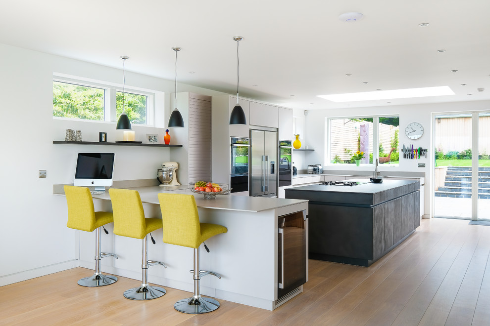 Große Moderne Küche in U-Form mit flächenbündigen Schrankfronten, Mineralwerkstoff-Arbeitsplatte, Kücheninsel, grauer Arbeitsplatte, grauen Schränken, Küchengeräten aus Edelstahl, braunem Holzboden und braunem Boden in Gloucestershire