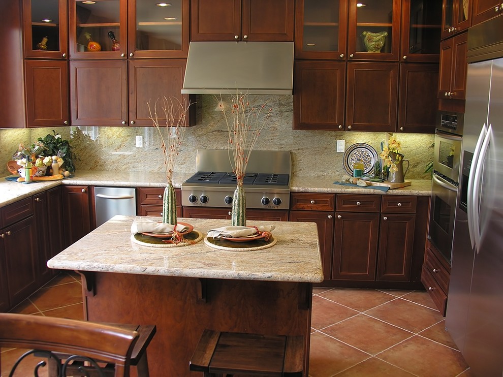 Immagine di una cucina classica con ante con riquadro incassato, ante in legno bruno, paraspruzzi beige, elettrodomestici in acciaio inossidabile, top in granito e pavimento in terracotta