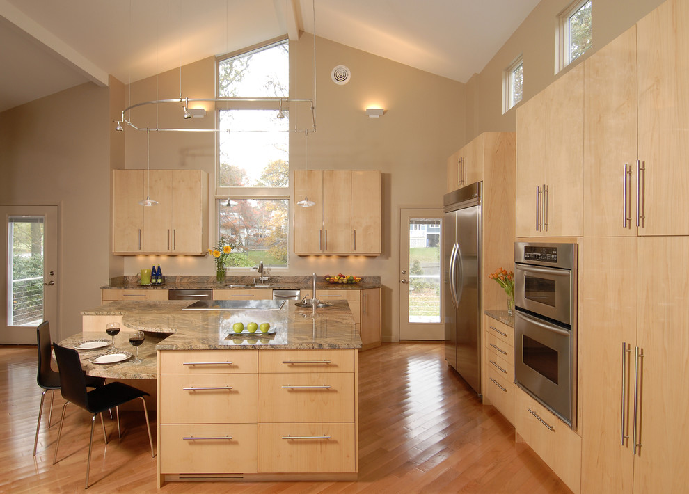 Imagen de cocina actual con electrodomésticos de acero inoxidable, armarios con paneles lisos, puertas de armario de madera clara y barras de cocina