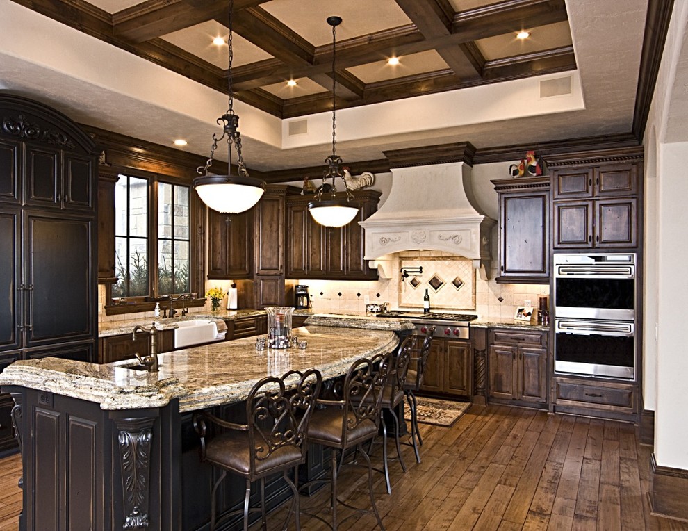 Large transitional l-shaped dark wood floor and brown floor kitchen photo in DC Metro with a farmhouse sink, raised-panel cabinets, dark wood cabinets, granite countertops, beige backsplash, limestone backsplash, paneled appliances, an island and multicolored countertops