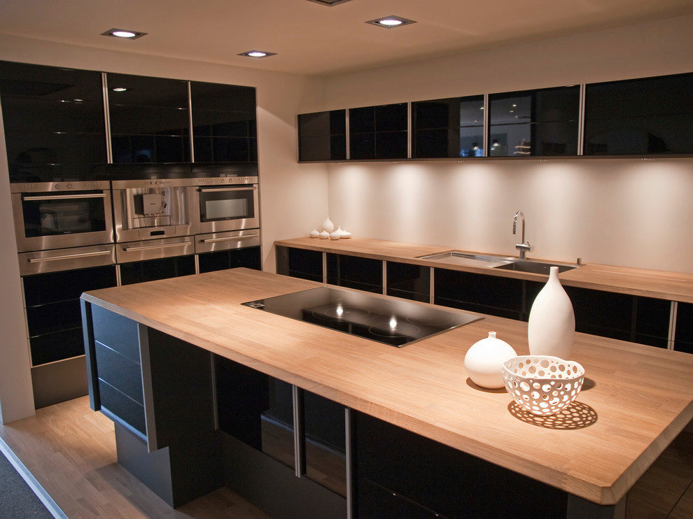 Exempel på ett mellanstort modernt linjärt kök med öppen planlösning, med en undermonterad diskho, luckor med glaspanel, svarta skåp, träbänkskiva, bambugolv och en köksö