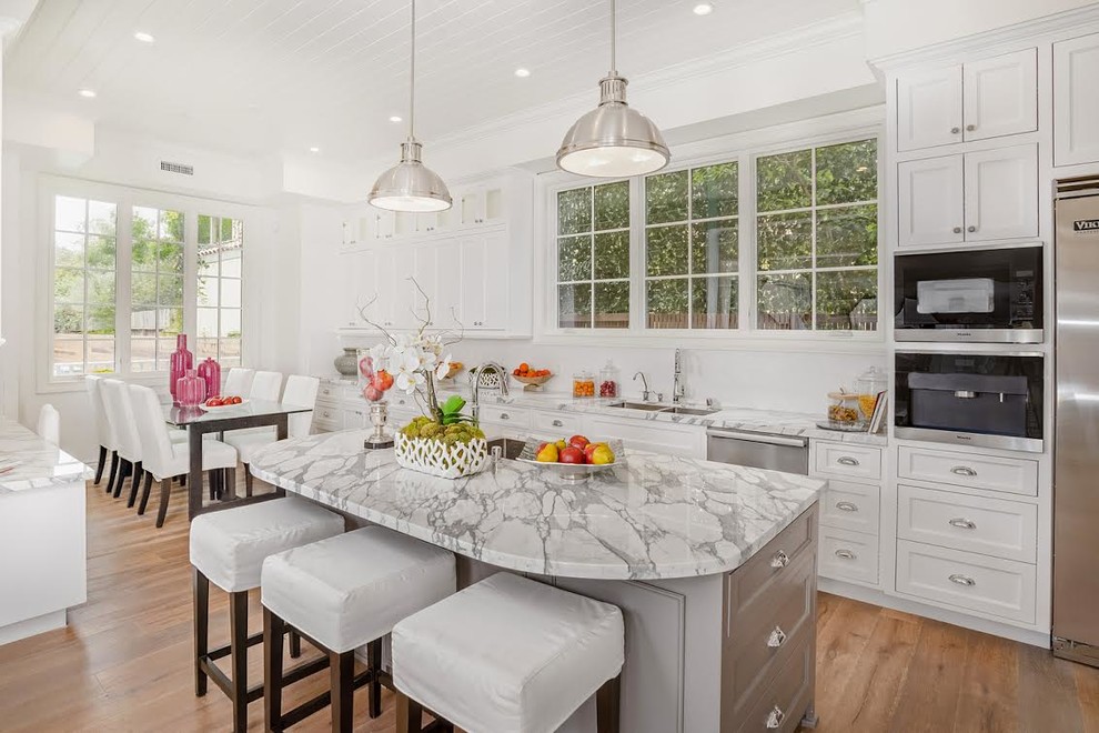 Large transitional u-shaped medium tone wood floor eat-in kitchen photo in Los Angeles with an undermount sink, white cabinets, white backsplash, stainless steel appliances, an island, recessed-panel cabinets, marble countertops and ceramic backsplash
