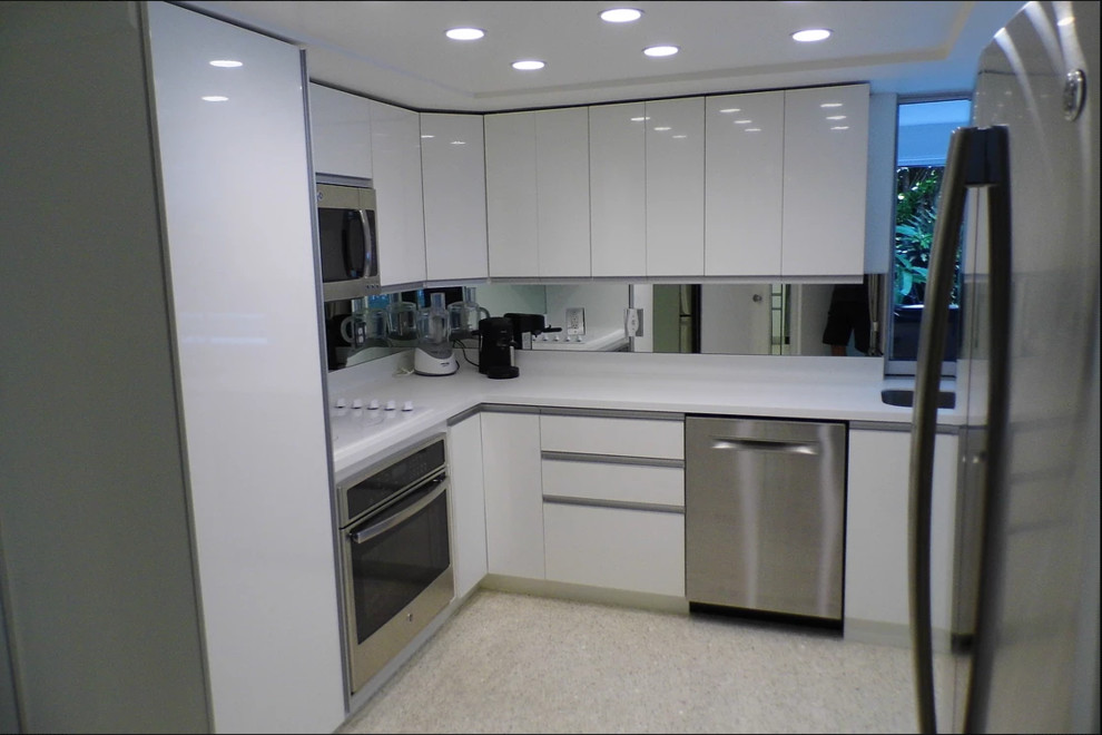 This is an example of a medium sized modern l-shaped open plan kitchen in Miami with a submerged sink, flat-panel cabinets, white cabinets, quartz worktops, mirror splashback, stainless steel appliances, an island and beige floors.