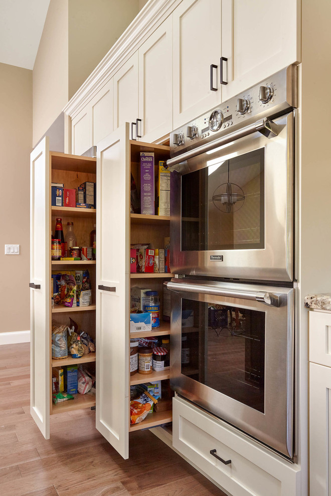 Photo of a large traditional l-shaped kitchen pantry in San Francisco with a belfast sink, shaker cabinets, white cabinets, granite worktops, beige splashback, ceramic splashback, stainless steel appliances, medium hardwood flooring, an island and brown floors.