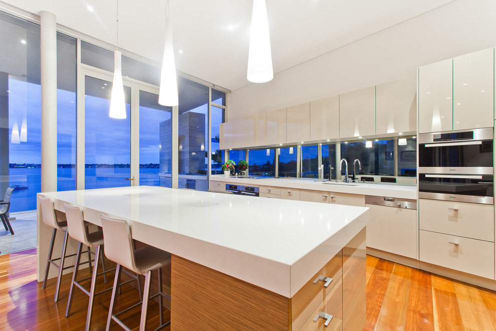 Einzeilige Moderne Küche mit Unterbauwaschbecken, flächenbündigen Schrankfronten, weißen Schränken, Küchengeräten aus Edelstahl, braunem Holzboden und Kücheninsel in Perth