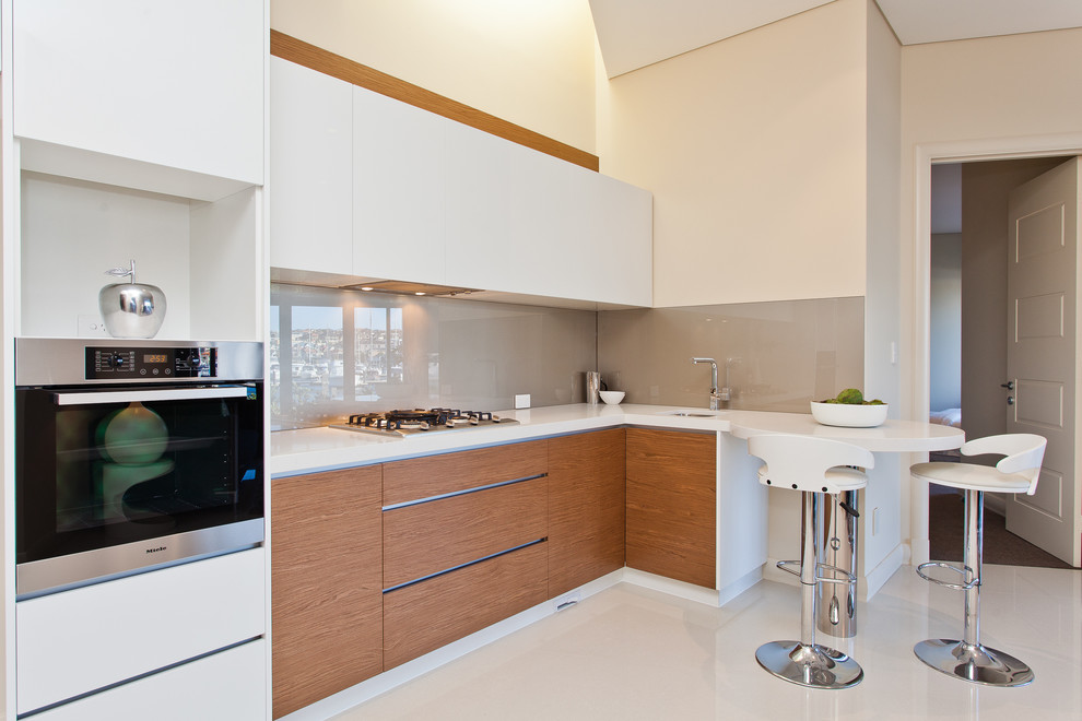 Photo of a small contemporary galley kitchen/diner in Perth with a submerged sink, flat-panel cabinets, white cabinets, beige splashback, glass sheet splashback, engineered stone countertops, stainless steel appliances and porcelain flooring.