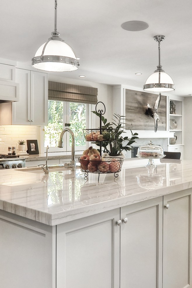 This is an example of a medium sized classic l-shaped kitchen/diner in Orange County with a submerged sink, recessed-panel cabinets, white cabinets, white splashback, stainless steel appliances, medium hardwood flooring, an island, metro tiled splashback, quartz worktops and white worktops.