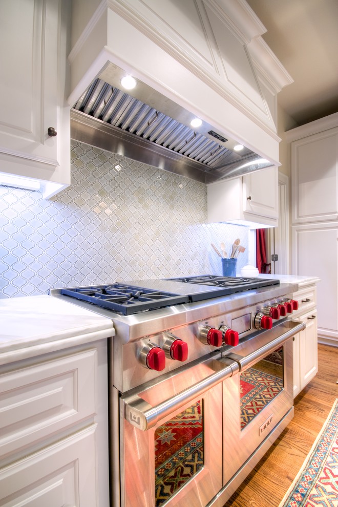 Inspiration for a large timeless l-shaped light wood floor eat-in kitchen remodel in Austin with raised-panel cabinets, white cabinets, marble countertops, white backsplash, glass tile backsplash, stainless steel appliances and an island