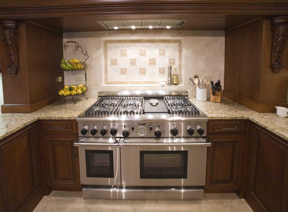 シカゴにあるトラディショナルスタイルのおしゃれなキッチン (レイズドパネル扉のキャビネット、濃色木目調キャビネット、ベージュキッチンパネル、シルバーの調理設備) の写真