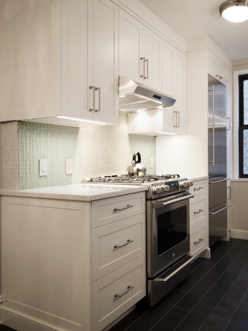 Modern apartment kitchen with premium RTA cabinets Canada—white shaker cabinetry, quartz countertop, pale glass-tile backsplash, stainless gas range and fridge, and dark plank flooring.