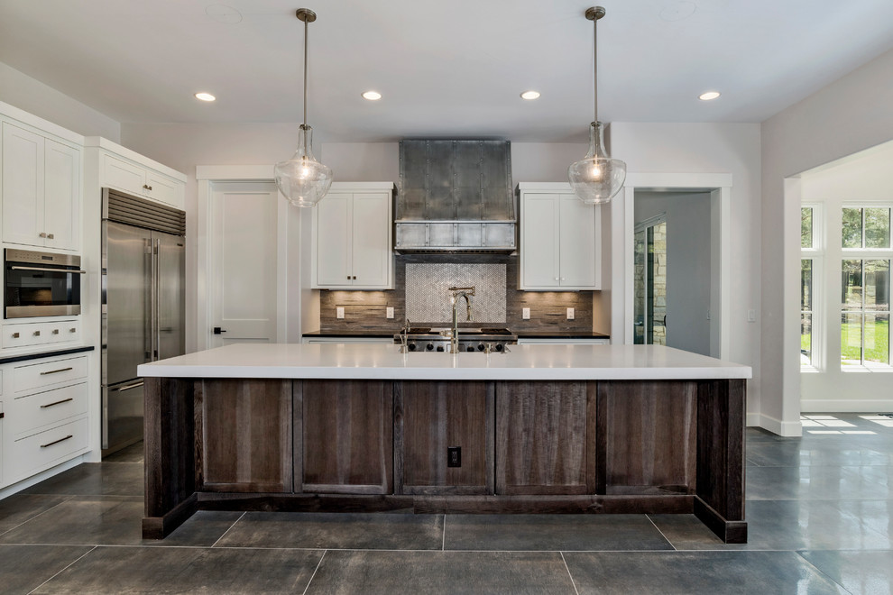 Example of a mid-sized country l-shaped slate floor and gray floor open concept kitchen design in Denver with a farmhouse sink, beaded inset cabinets, white cabinets, solid surface countertops, gray backsplash, stone tile backsplash, stainless steel appliances, an island and white countertops