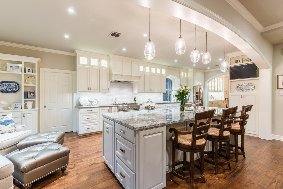 Example of a large transitional single-wall medium tone wood floor eat-in kitchen design in Austin with an undermount sink, raised-panel cabinets, white cabinets, granite countertops, gray backsplash, porcelain backsplash, stainless steel appliances and an island