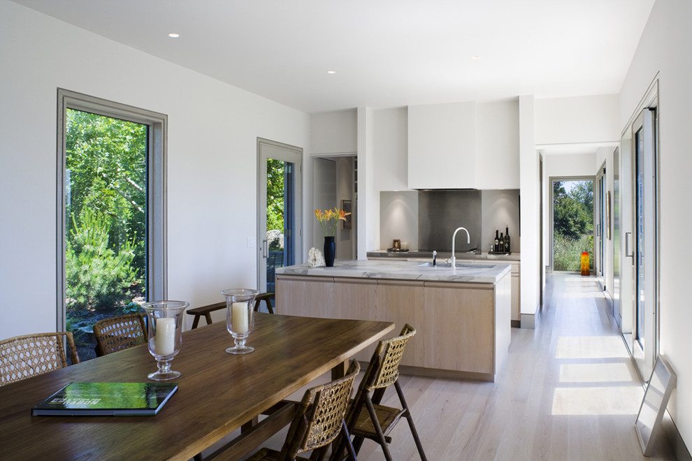 Idée de décoration pour une petite cuisine américaine parallèle minimaliste en bois clair avec un placard à porte plane, plan de travail en marbre, une crédence grise, parquet clair et îlot.