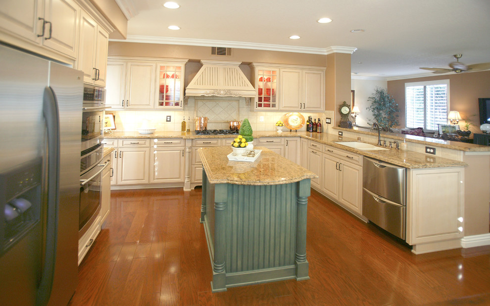 Example of a large classic u-shaped medium tone wood floor eat-in kitchen design in Orange County with a double-bowl sink, recessed-panel cabinets, white cabinets, granite countertops, white backsplash, ceramic backsplash, stainless steel appliances and an island
