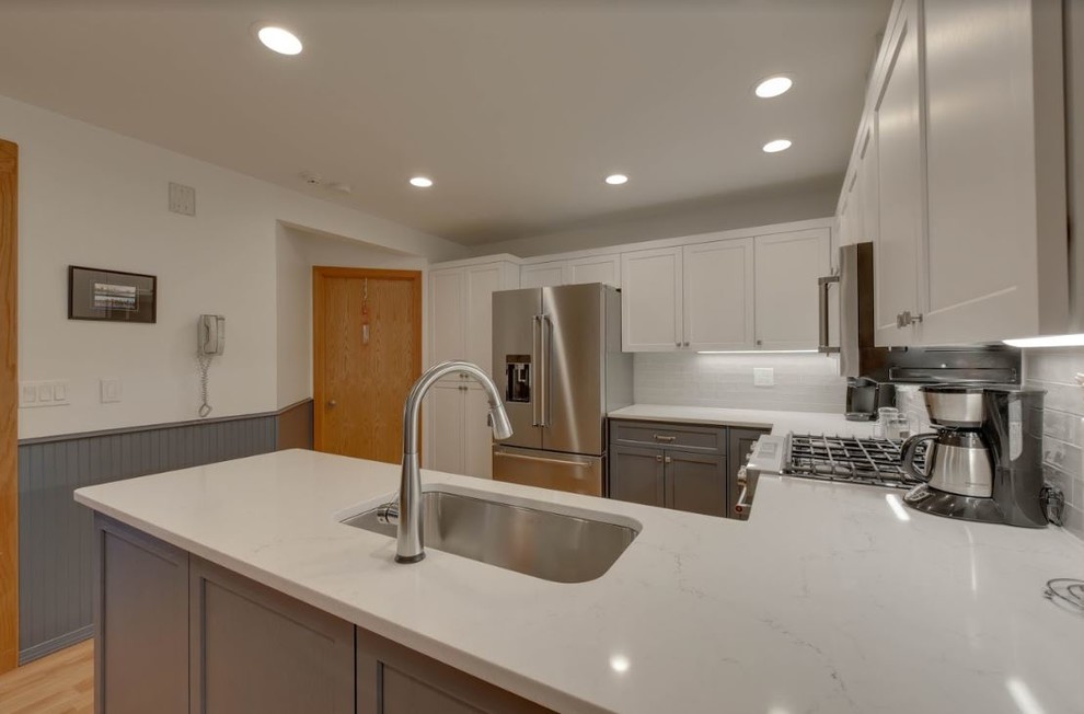 Inredning av ett mellanstort vit vitt kök, med en undermonterad diskho, skåp i shakerstil, vita skåp, bänkskiva i kvarts, vitt stänkskydd, stänkskydd i tunnelbanekakel, rostfria vitvaror, ljust trägolv, en halv köksö och orange golv