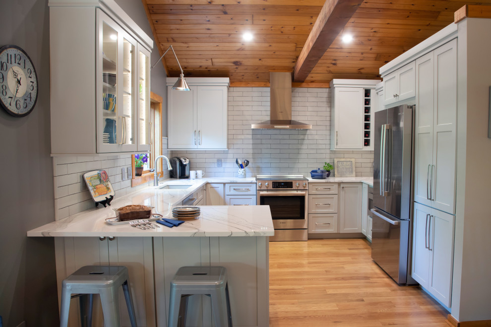 This is an example of a medium sized classic u-shaped enclosed kitchen in Milwaukee with a submerged sink, recessed-panel cabinets, grey cabinets, engineered stone countertops, white splashback, porcelain splashback, stainless steel appliances, medium hardwood flooring, a breakfast bar, brown floors, white worktops and a timber clad ceiling.