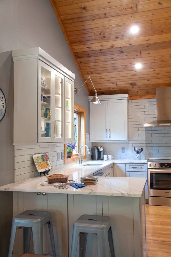 Mid-sized elegant u-shaped medium tone wood floor, brown floor and shiplap ceiling enclosed kitchen photo in Milwaukee with an undermount sink, recessed-panel cabinets, gray cabinets, quartz countertops, white backsplash, porcelain backsplash, stainless steel appliances, a peninsula and white countertops