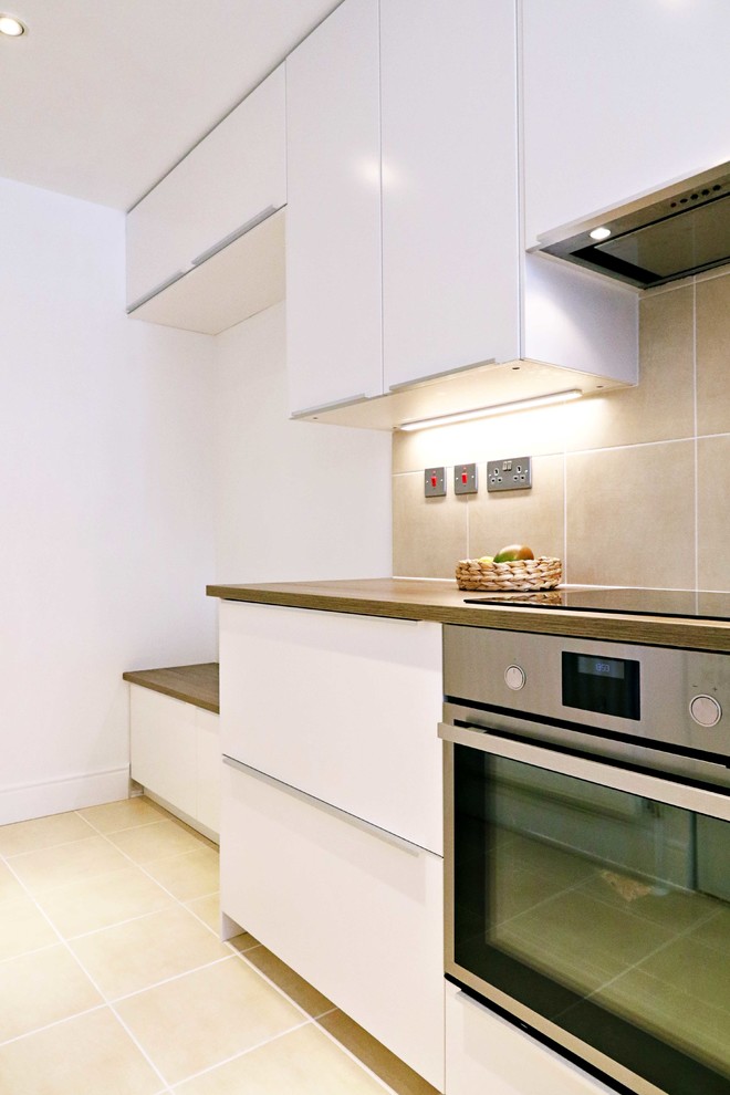 This is an example of a medium sized modern u-shaped kitchen/diner in London with a single-bowl sink, laminate countertops, beige splashback, ceramic splashback, white appliances, ceramic flooring, no island, beige floors and brown worktops.