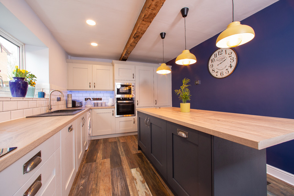 Bild på ett mellanstort funkis l-kök, med en dubbel diskho, skåp i shakerstil, vitt stänkskydd, stänkskydd i tunnelbanekakel, rostfria vitvaror, mörkt trägolv, en köksö och brunt golv