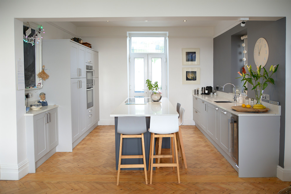 Modern inredning av ett stort vit vitt kök och matrum, med en undermonterad diskho, skåp i shakerstil, grå skåp, bänkskiva i koppar, rostfria vitvaror, mellanmörkt trägolv och en köksö