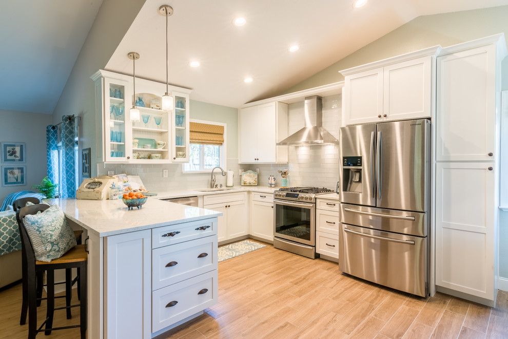 Example of a mid-sized beach style u-shaped ceramic tile eat-in kitchen design in Sacramento with an undermount sink, glass-front cabinets, white cabinets, marble countertops, white backsplash, glass tile backsplash, stainless steel appliances and a peninsula