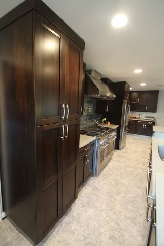 This is an example of a contemporary l-shaped kitchen in DC Metro with shaker cabinets, dark wood cabinets, engineered stone countertops, grey splashback, metro tiled splashback, stainless steel appliances, ceramic flooring and grey floors.