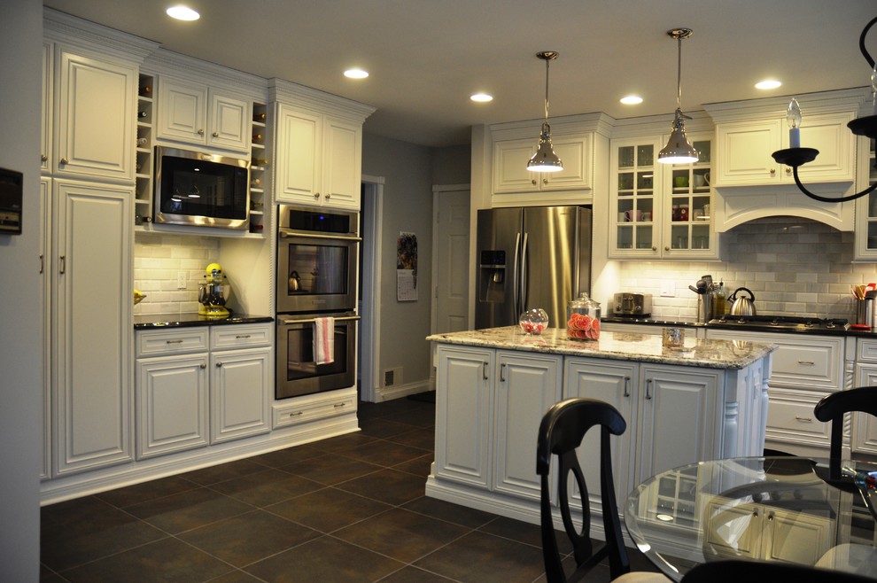 Exempel på ett mellanstort klassiskt l-kök, med en undermonterad diskho, luckor med upphöjd panel, vita skåp, granitbänkskiva, vitt stänkskydd, stänkskydd i stenkakel, rostfria vitvaror, skiffergolv, en köksö och svart golv