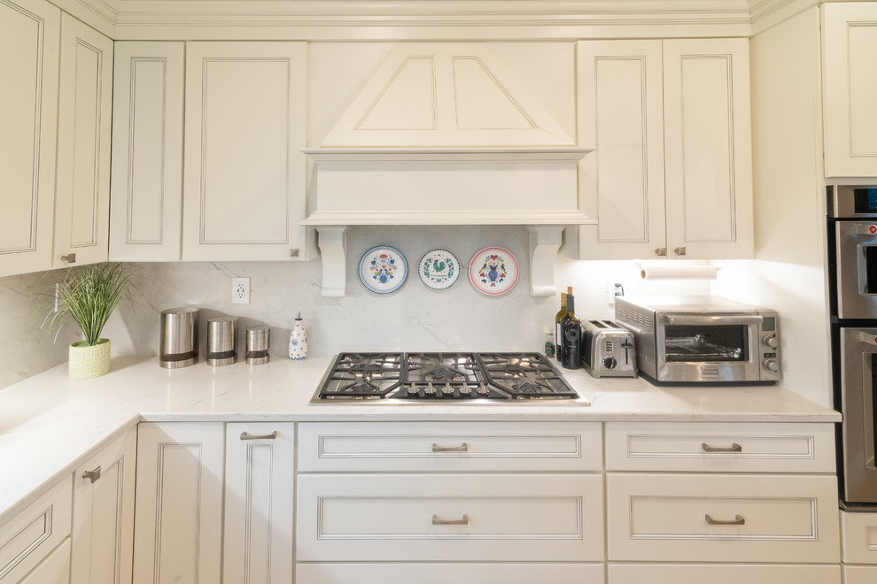 Modern inredning av ett stort vit vitt kök, med en dubbel diskho, luckor med infälld panel, vita skåp, marmorbänkskiva, vitt stänkskydd, stänkskydd i marmor, rostfria vitvaror, klinkergolv i keramik, en köksö och beiget golv
