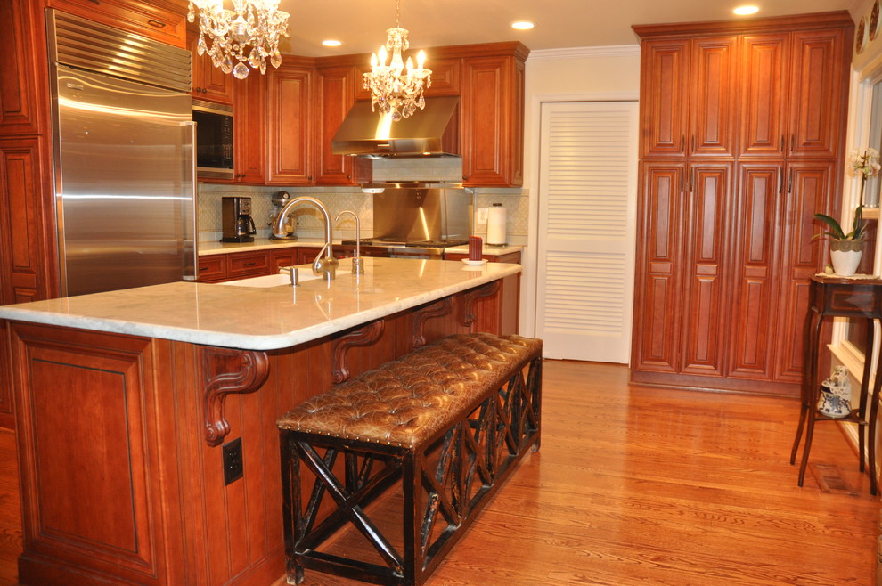 Example of a mid-sized classic l-shaped medium tone wood floor and brown floor enclosed kitchen design in DC Metro with a farmhouse sink, stainless steel appliances, beige backsplash, glass tile backsplash, raised-panel cabinets, medium tone wood cabinets, granite countertops and an island