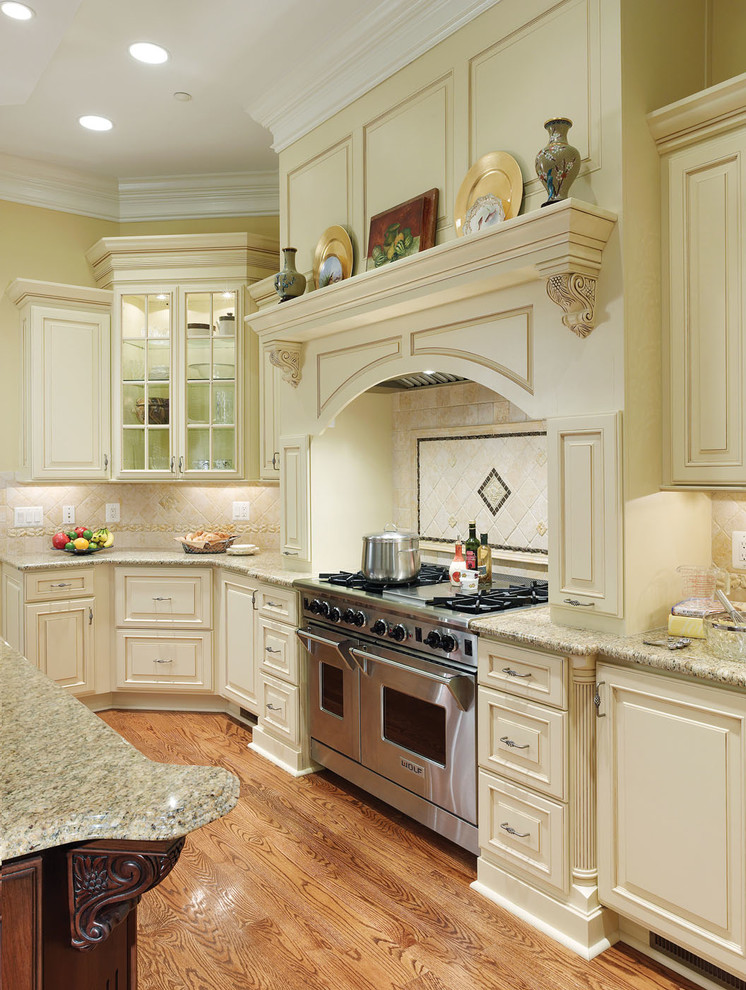 Foto på ett stort vintage kök, med luckor med upphöjd panel, vita skåp, granitbänkskiva, beige stänkskydd, stänkskydd i stenkakel, integrerade vitvaror, mellanmörkt trägolv, en köksö och brunt golv