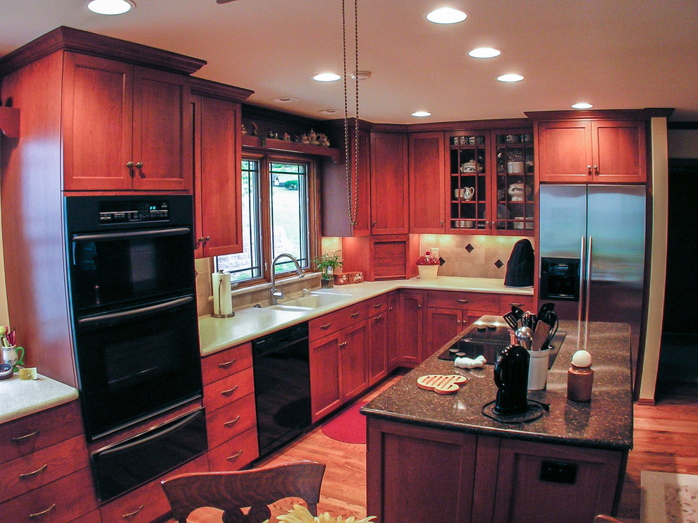 Example of a mid-sized classic l-shaped medium tone wood floor enclosed kitchen design in St Louis with a double-bowl sink, shaker cabinets, red cabinets, quartz countertops, beige backsplash, ceramic backsplash, black appliances and an island