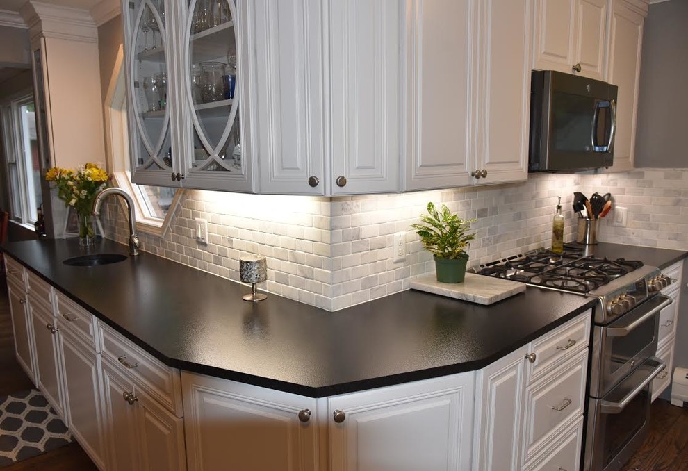 Example of a large classic l-shaped dark wood floor and brown floor enclosed kitchen design in Chicago with an undermount sink, raised-panel cabinets, white cabinets, granite countertops, gray backsplash, subway tile backsplash, white appliances and an island