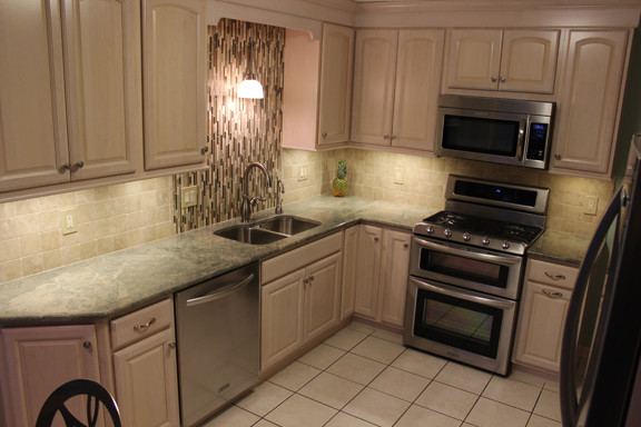 Example of a classic ceramic tile kitchen design in Cleveland with a drop-in sink, raised-panel cabinets, beige cabinets, granite countertops, brown backsplash, stone tile backsplash and stainless steel appliances