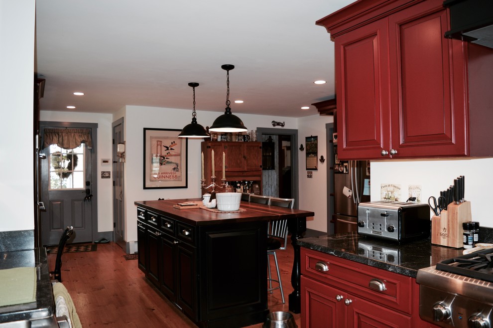 This is an example of a large country u-shaped kitchen in Boston with a belfast sink, raised-panel cabinets, red cabinets, composite countertops, stainless steel appliances, light hardwood flooring and an island.