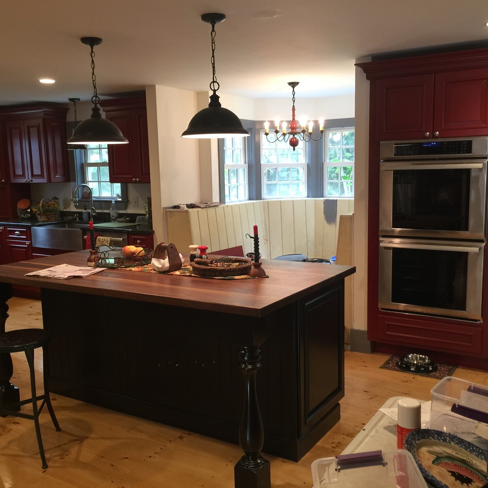 Große Country Küche in U-Form mit Landhausspüle, profilierten Schrankfronten, roten Schränken, Mineralwerkstoff-Arbeitsplatte, Küchengeräten aus Edelstahl, hellem Holzboden und Kücheninsel in Boston
