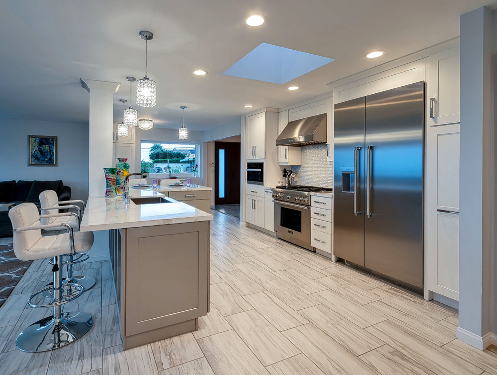 Medium sized modern u-shaped open plan kitchen in San Diego with a belfast sink, shaker cabinets, white cabinets, engineered stone countertops, glass tiled splashback, stainless steel appliances, porcelain flooring, an island, grey floors and white worktops.