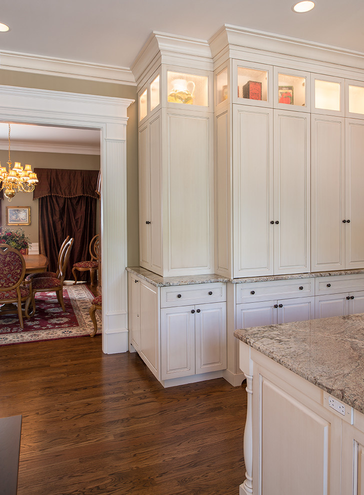 Klassisk inredning av ett stort kök med öppen planlösning, med en undermonterad diskho, vita skåp, granitbänkskiva, rostfria vitvaror, mellanmörkt trägolv, en köksö, brunt golv, beige stänkskydd och stänkskydd i keramik