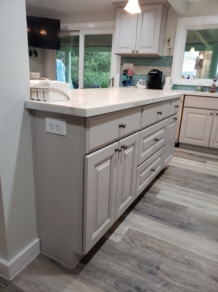 Photo of a medium sized coastal galley kitchen/diner in Houston with a double-bowl sink, raised-panel cabinets, grey cabinets, engineered stone countertops, green splashback, glass tiled splashback, stainless steel appliances, vinyl flooring, an island, grey floors and white worktops.